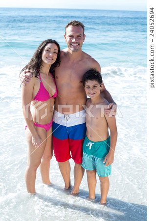 Smiling family standing wearing swinwear at beach  24052694