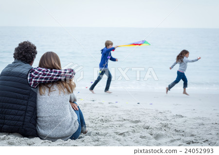 Couple sitting while playful children at sea shore Couple sitting while playful children at sea shore 24052993