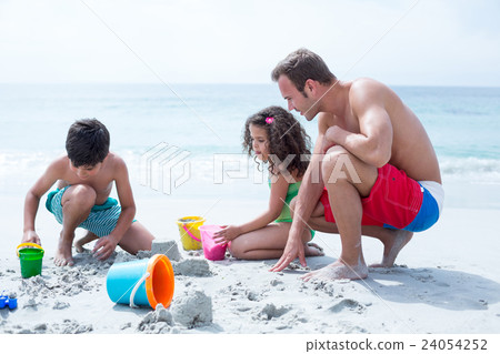 Father helping children building sand castle at beach Father helping children building sand castle at beach 24054252
