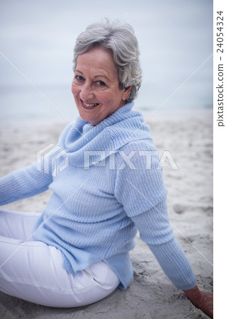 Portrait of happy senior woman sitting on beach 24054324