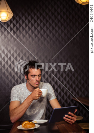 Hipster man using tablet with coffee and pastry Hipster man using tablet with coffee and pastry 24054441