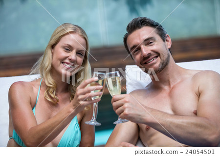 Couple sitting on sun lounger toasting champagne Couple sitting on sun lounger toasting champagne 24054501