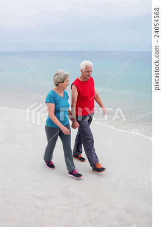 Senior couple holding hands and walking on the beach Senior couple holding hands and walking on the beach 24054568