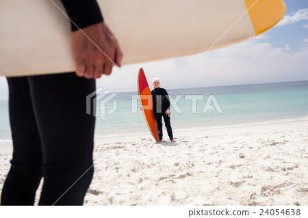 Senior woman in wetsuit holding surfboard on beach 24054638