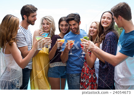 Group of friends holding a glass of cocktail near the pool 24054673