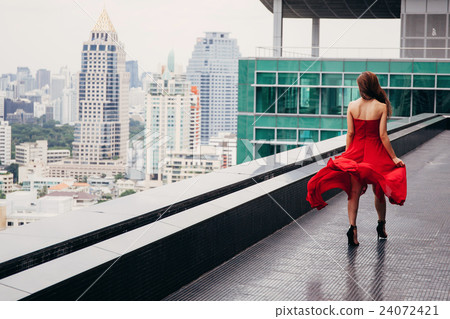 Woman in red walking on rooftop with cityscape Woman in red walking on rooftop with cityscape 24072421