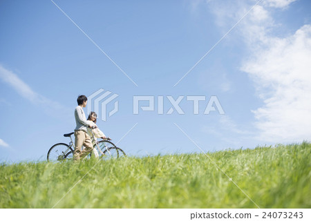 A couple pushing a bicycle in the meadow 24073243