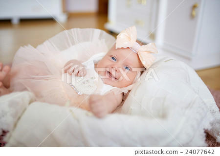 Smiling babygirl in peach dress lies in the basket 24077642