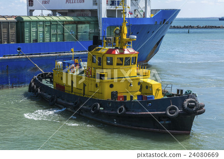 Yellow tugboat assisting large cargo ship 24080669