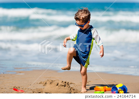 Cute boy demolishing sand castle 24164714