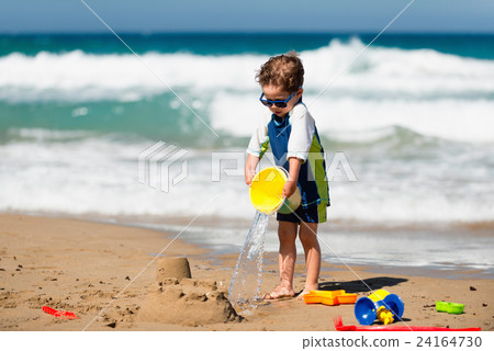 Little boy pouring water on sand castle 24164730