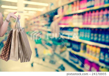 Holding shopping bags by hand on Supermarket with Abstract blurred photo of store with trolley in department store bokeh background 24178935