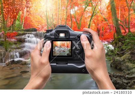 Hands holding the camera which taking photo of Beautiful waterfall with soft focus and rainbow in the forest 24180310