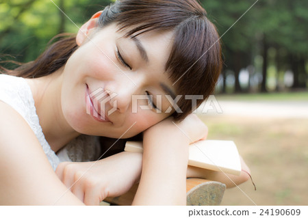 A woman relaxing while reading a book with a park bench 24190609
