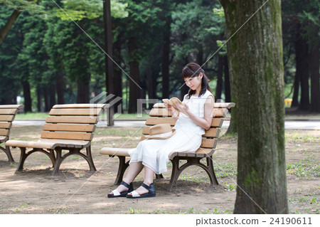 A woman reading a book on a park bench 24190611