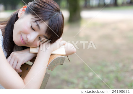 A woman reading a book while relaxing at a park bench 24190621