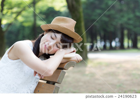 讀書的婦女,當放鬆在公園長椅時 讀書的婦女,當放鬆在公園長椅時 24190623