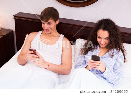 Couple with smartphones in bed. 24209665