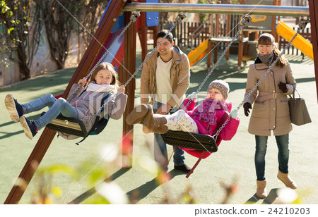 Parents watching little daughters swinging Parents watching little daughters swinging 24210203