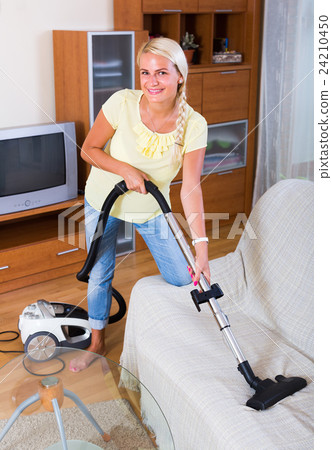 Blonde girl hoovering in living room . 24210450
