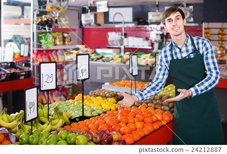 Male seller posing with apples, tangerines and bananas in store 24212887