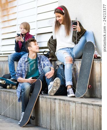 Three teenagers with phones outdoors . 24213377