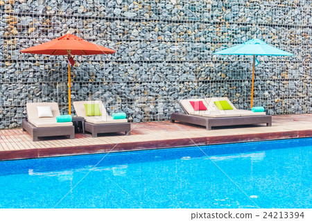 Umbrella and chair around swimming pool 24213394