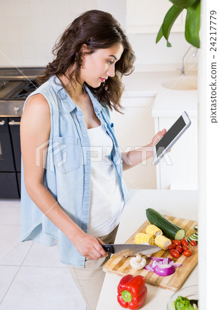 Young woman using digital tablet while chopping vegetables 24217779