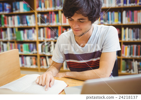 Young student sitting at desk reading a book Young student sitting at desk reading a book 24218137