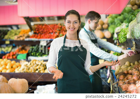 Friendly positive sellers having vegetables and fruits on displays Friendly positive sellers having vegetables and fruits on displays 24245272