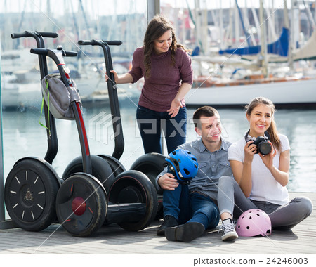 Positive friends posing near segways on shore 24246003