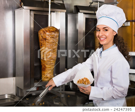 Professional female cook with grilled meat on spit for kebab 24247395