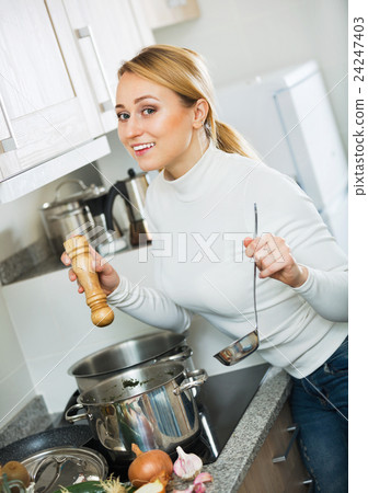 Smiling long-haired girl cooking soup at kitchen stove Smiling long-haired girl cooking soup at kitchen stove 24247403