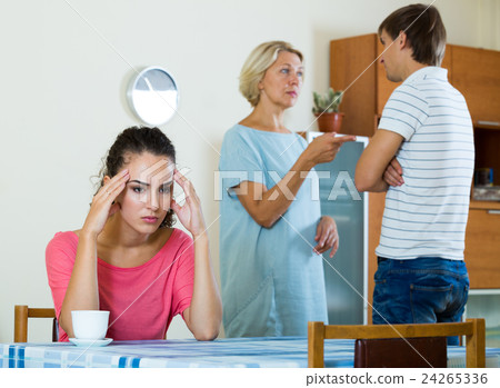 Sad young woman watching husband and mother having fight Sad young woman watching husband and mother having fight 24265336