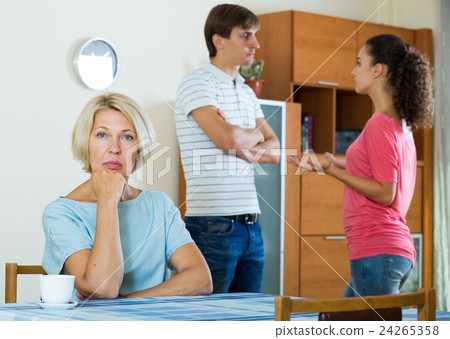 Mature woman watching young family couple quarrel at home Mature woman watching young family couple quarrel at home 24265358