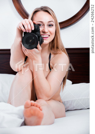 Laughing woman lying in the bed and holding a camera 24266252