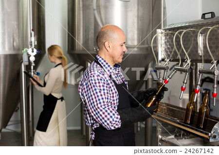 Man employee bottling beer in glass bottles Man employee bottling beer in glass bottles 24267142