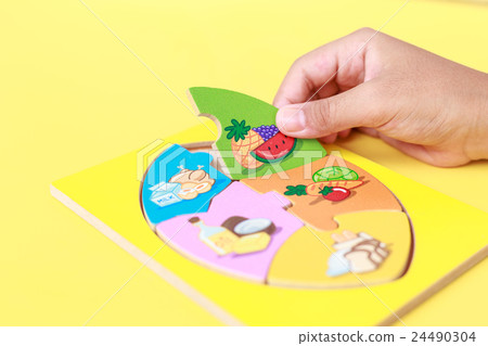 Hand of kid holding wooden jigsaw of the 5 food Groups. Child development concept 24490304