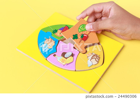 Hand of kid holding wooden jigsaw of the 5 food Groups. Child development concept Hand of kid holding wooden jigsaw of the 5 food Groups. Child development concept 24490306