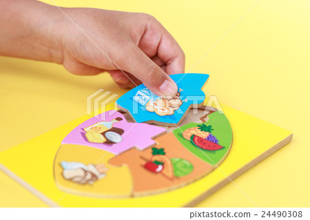 Hand of kid holding wooden jigsaw of the 5 food Groups. Child development concept Hand of kid holding wooden jigsaw of the 5 food Groups. Child development concept 24490308