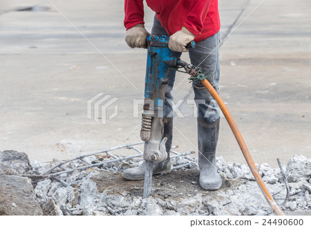 Construction worker removes excess concrete with drilling machine 24490600