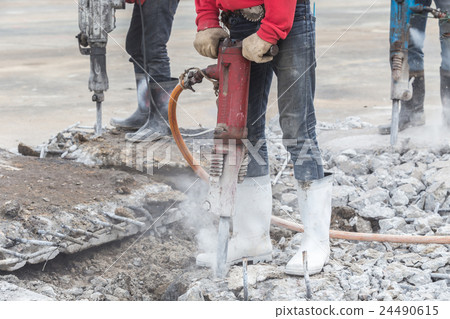 Construction worker removes excess concrete with drilling machine 24490615