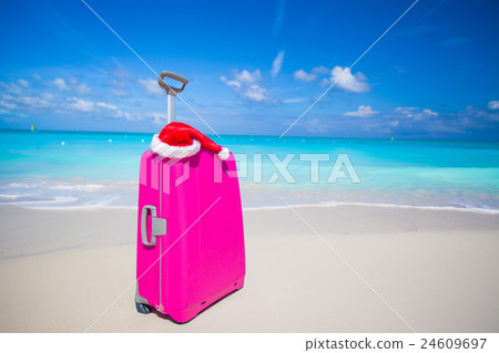 Pink suitcase and Santa Claus hat on white sand 24609697