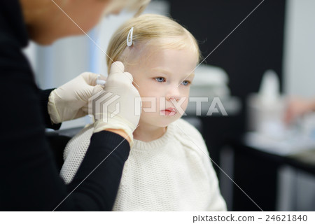 Adorable little girl having ear piercing process in beauty center 24621840
