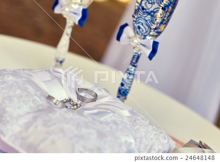 Wedding rings on a cushion near the glasses of 24648148