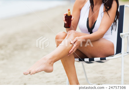woman spraying sunscreen oil to her skin on beach 24757306