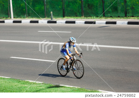 Female cyclist rides a racing bike on road Female cyclist rides a racing bike on road 24759802