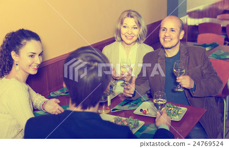 Four adults with wine and dinner laughing in restaurant 24769524
