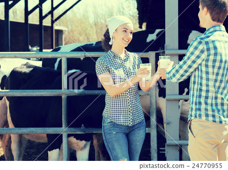 Cheerful boy and girl farmers standing with in the cow hangar and showing fresh milk Cheerful boy and girl farmers standing with in the cow hangar and showing fresh milk 24770955
