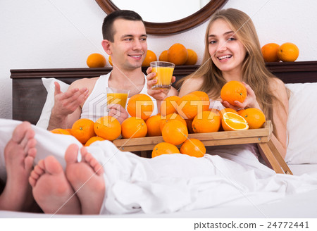 Couple in bed with orange fruits. 24772441